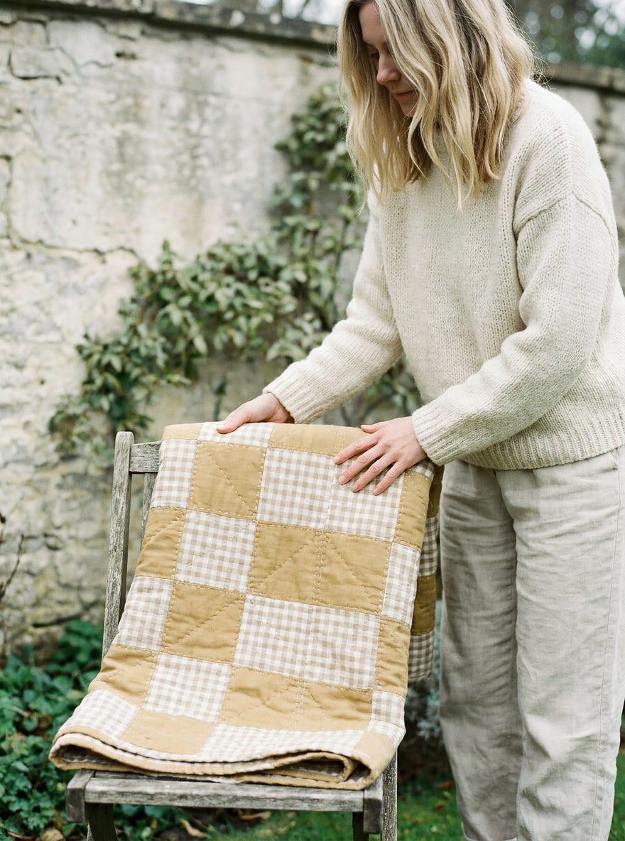 A hand-pieced sage and ochre patchwork quilt held in soft window light, the hand-quilting stitches visible.