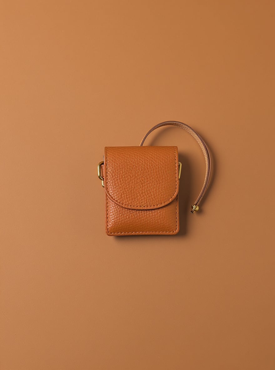 The Cognac Key Wristlet on a plain backdrop: pebbled cognac leather with a brass D-ring and looped wrist strap.